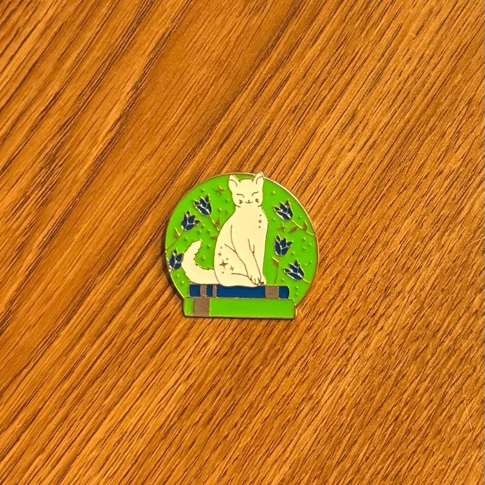 Women’s Accessories White Cat Sitting on Books Enamel Pin with Green Background